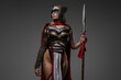 Studio shot of wild female warrior from past with painted face holding spear isolated on grey background.