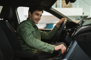 Happy young Caucasian man test driving new car before purchase at modern automobile dealership, copy space