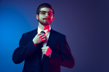 Portrait of young stylish man in business suit posing isolated on dark blue studio background. Concept of human emotions, facial expression, sales, ad, fashion and beauty