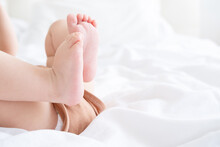Close Up Baby Barefooted Legs Feet Lying On White Bed Linen. Neutral Pastel Light Color Tones