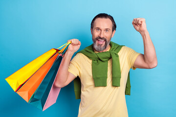 Sticker - Portrait of delighted satisfied man raise fist hold packages luck isolated on blue color background