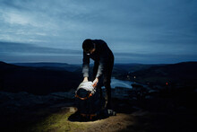 Male Hiker With Headlamp And Backpack Preparing To Camp On Hill At Night, Bamford Edge, England
