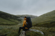Male Hiker With Backpack Resting On Rock In Grassy Remote Landscape, Red Tarn, England
