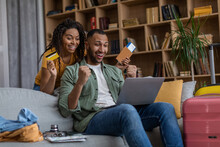 Overjoyed Black Tourists Couple Using Laptop And Credit Card, Booking Hotel Room Online, Ready For Vacation Trip