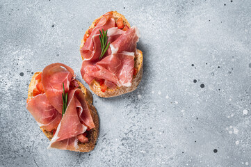 Wall Mural - Spanish Tapas with tomatoes and cured Slices of jamon iberico ham, fresh toasts. Gray background. Top view. Copy space