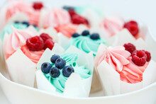Appetizing And Delicious Muffins With Pink And Blue Cream Cheese Are Decorated With Fresh Wild Raspberries And Blueberries. Sweet Tasty Desserts On White Plate. Boy Or Girl? Close-up, White Background