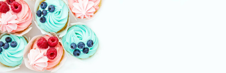 Appetizing and delicious muffins with pink and blue cream cheese are decorated with fresh wild raspberries and blueberries. Sweet tasty desserts on white plate. Boy or girl? White copy space. Flat lay