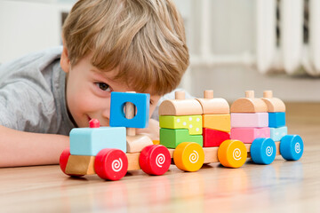 boy sitting on the floor and playing with wooden colorful block train. pre-school employment. montes