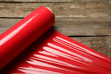 Wall Mural - Roll of red plastic stretch wrap on wooden background, closeup