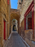 Fototapeta Uliczki - A cobblestone alley between picturesque old stone houses with reddish doors and windows. Pirgi, Chios island, Greece