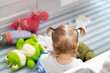 baby girl with two pigtails have fun with plush toys at natural home background, view from behind