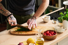 Horizontal Medium Section Shot Of Unrecognizable Chef With Tattooes On Arms Chopping Fresh Cilantro Or Parsley On Cutting Board