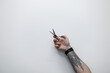© alones - Professional hairdresser holds a tattooed scissors in his hand against a white background. Creative hairstyles, concept. Barbershop