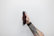 © alones - The male hand of a professional hairdresser with a tattoo is holding a haircutting machine against a white background. Barber shop and haircuts, concept idea