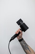 © alones - Male hand with a tattoo is holding a black modern hair dryer against a white background. Professional barber in a barber shop. Creative work