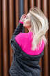 Beautiful young fresh blonde girl model with healthy hair in a fashionable pink sweater and jacket walking in the city. Fashion urban female portrait