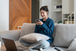 © Natee Meepian - Attractive smiling woman using smart phone while sitting on the sofa at home. Communication and coziness concept