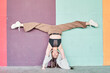 © Oscar - Full length powerful woman in casual wear performing handstand with split near colorful wall