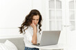 © etonastenka - Serious focused young woman using laptop, checking news on internet, sitting on sofa, solving problems at remote work