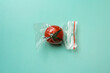 Red tomato in a zip bag on a green background, the concept of excess food packaging