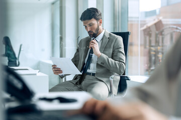 Handsome young entrepreneur working with computer while reading some documents in modern startup office.