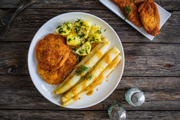 Wall Mural - Fried schnitzel and white boiled asparagus with potato served on wooden table
