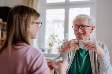 Wall Mural - Adult daughter visiting her senior father at home and having coffee together, talking.