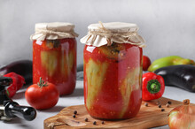Peppers Stuffed With Eggplant And Onions, In Tomato Sauce, In Two Glass Jars On Light Gray Background