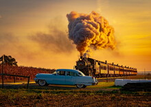 A View Of An Antique Steam Passenger Train Approaching At Sunrise With A Full Head Of Steam And Smoke Traveling Thru Farmlands With An Antique Car Waiting For It To Pass