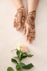 Wall Mural - Female hands with henna tattoo and beautiful rose flower on light background, closeup