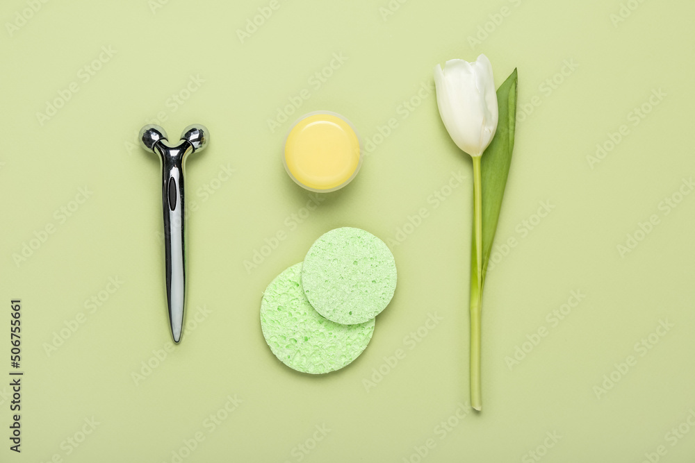 Facial massage tool with cream, sponges and tulip on green background. Mother's Day celebration