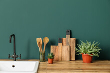 Wooden Cutting Boards, Spatulas, Sink And Houseplants On Counter Near Green Wall