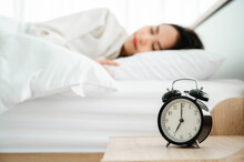 Young Asian Woman Happy Sleep At Morning In Bedroom. Closeup Of Alarm Clock On White Bed