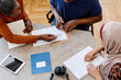 © pressmaster - High angle view shot of two young women helping mature Black man to correct mistake during English language class for immigrants