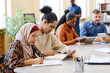 © pressmaster - Group of ethnically diverse people having language lesson for immigrants sitting at table doing task with use of digital tablets