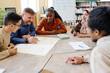 © pressmaster - English language teacher sitting at table with his students checking spelling of words on poster they created
