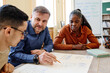 © pressmaster - Mature English language teacher sitting at table with his students asking them questions during lesson