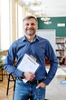 © pressmaster - Vertical medium shot of joyful mature Caucasian man teaching English language holding clipboard with grammar tests smiling at camera