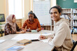 © pressmaster - Young Black man sitting at table enjoying learning English language at school for immigrants smiling at camera