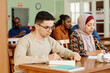 © pressmaster - Group of immigrant students in international class sitting at desk reading and making notes during lesson