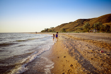 Wall Mural - free summer vacation and happy children. Sister girls in swimsuits run and play on the seashore and mountains,