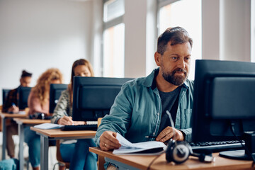 mature student uses desktop pc while learning in classroom.