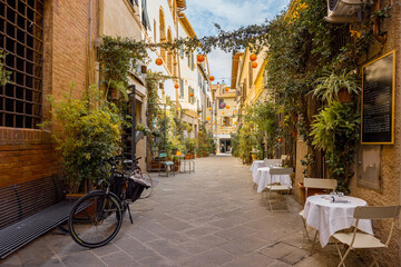 Wall Mural - Beautifully landscaped narrow street with restaurant tables in the old town of Grosseto, in Maremma region of Italy. Cozy city view of the old Italian town
