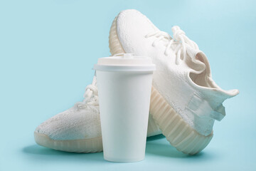 Coffee to go. White sneakers and a white paper cup with coffee