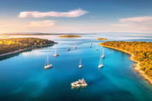Aerial View Of Beautiful Yachts And Boats On The Sea At Sunset In Summer. Adriatic Sea, Kamenjak, Croatia. Top View Of Luxury Yachts, Sailboats, Lagoon, Clear Blue Water, And Green Forest. Travel