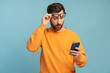 © NFstock - Mobile connection. Portrait of shocked astonished man reading post on social network using cell phone, chatting looking surprised. Indoor studio shot isolated on blue background