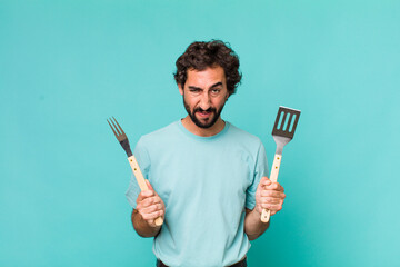 Wall Mural - young adult hispanic crazy man with barbecue tools