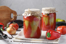 Peppers Stuffed With Eggplant And Onions, In Tomato Sauce, In Two Glass Jars On Gray Background