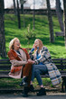 A grandmother is laughing and having fun with her adolescent granddaughter while sitting on the park bench.