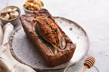 Wall Mural - Chocolate banana bread with walnuts on a white plate with brown rim and ingredients on a grey neutral background